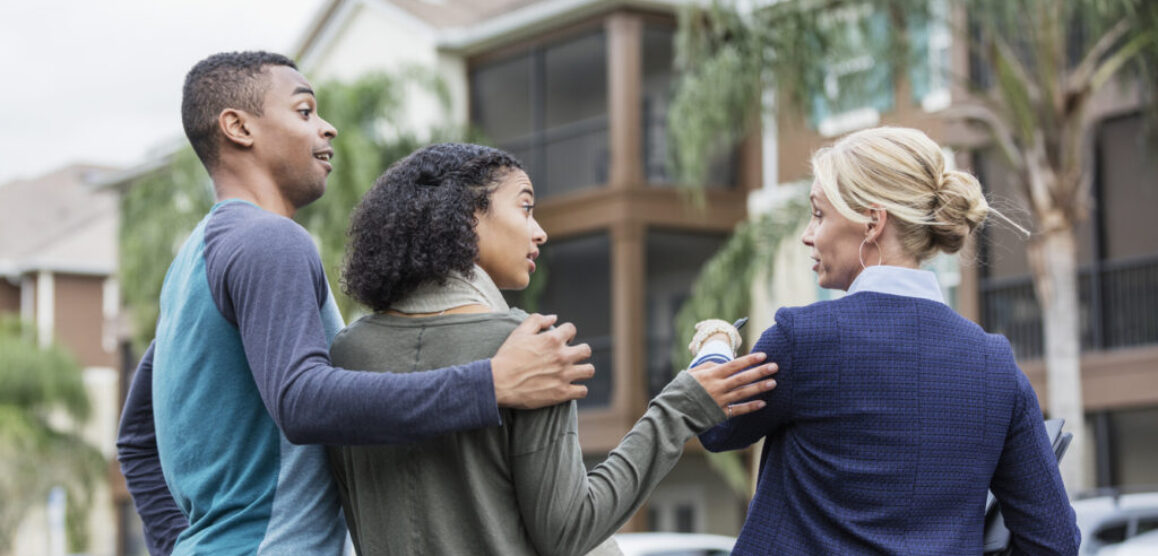 Young couple with real estate agent outside building